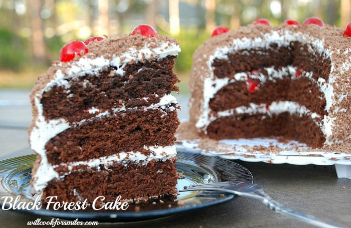 Black Forest Cake slice on a black plate with a fork to the right and the rest of the cake in the background