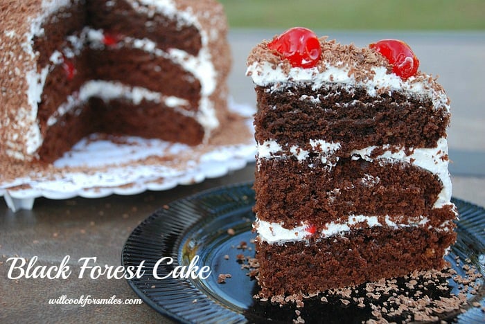 Black Forest Cake slice on a black plate and the rest of the cake in the background