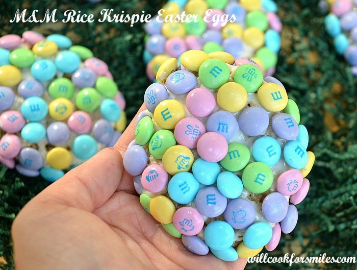 picture of hand holding rice crispy treat egg with m&ms covering it 2 partial crispies in background