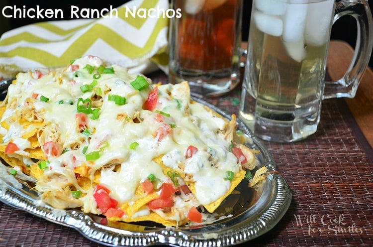 front shot of chicken ranch nachos on silver platter with 2 drinks in glasses in background to the right