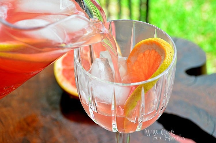 pouring grapefruit sangria into wine glass with ice and slice of grapefruit