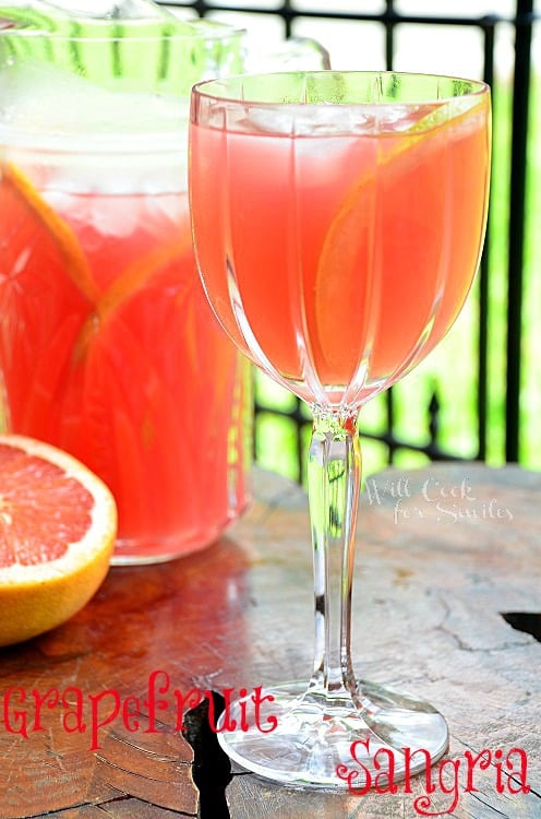 Grapefruit Sangria in a wine glass with a half a grapefruit in the background and the rest in a pitcher