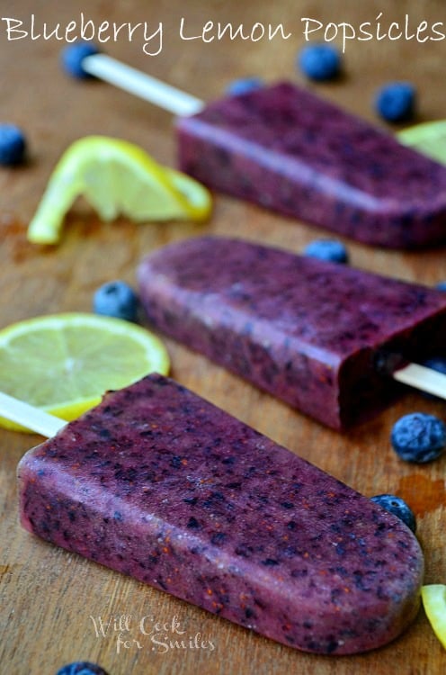 Blueberry lemon popsicles on a wood cutting board with slices lemons and blueberries