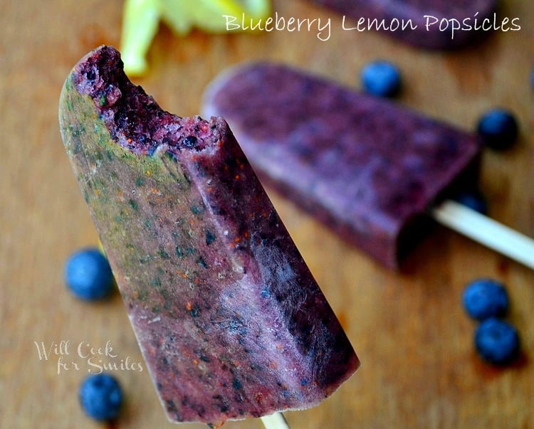 blueberry lemon popsicle with 1 bite held up and additional pop resting on table below