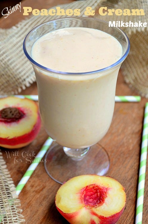 peaches and cream milkshake in a glass with peaches around it and green and white straws