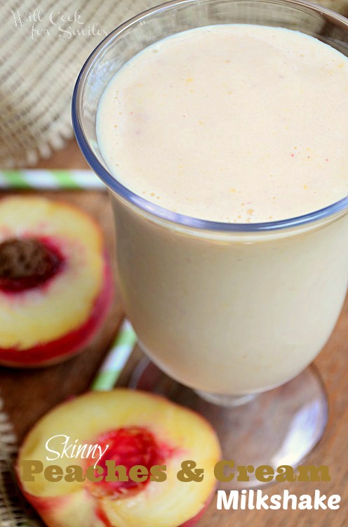 peaches and cream milkshake in a glass with peaches around it and green and white straws