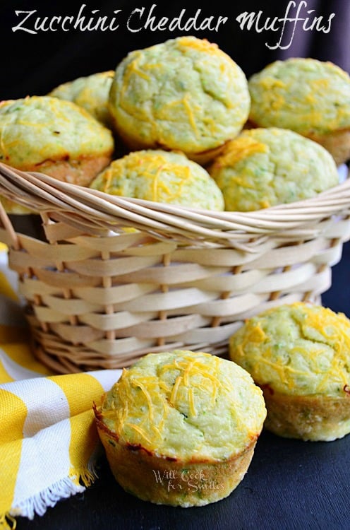 Cheddar Zucchini Muffins in a basket with two on the table top and a yellow and white kitchen towel
