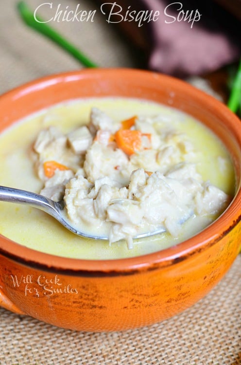 reddish orange clay bowl filled with chicken bisque soup on a brown placemat with spoon in soup