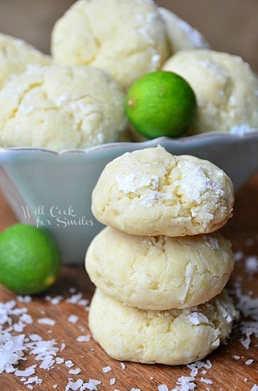 key lime cookies stacked up with some in a bowl behind the cookies and coconut shavings around the bottom