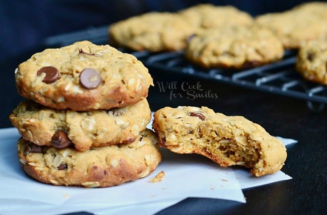 Cookies stacked up on wax paper on a black counter top with a bite out of one of them