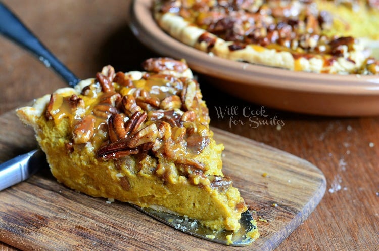 Pecan Caramel Pumpkin Cheesecake Pie slice on a wood cutting board with the rest of the pie in a brown pie pan