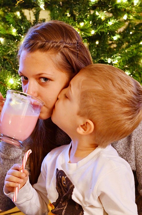 girl drinking the hot chocolate and boy kissing her check while holding candy cane