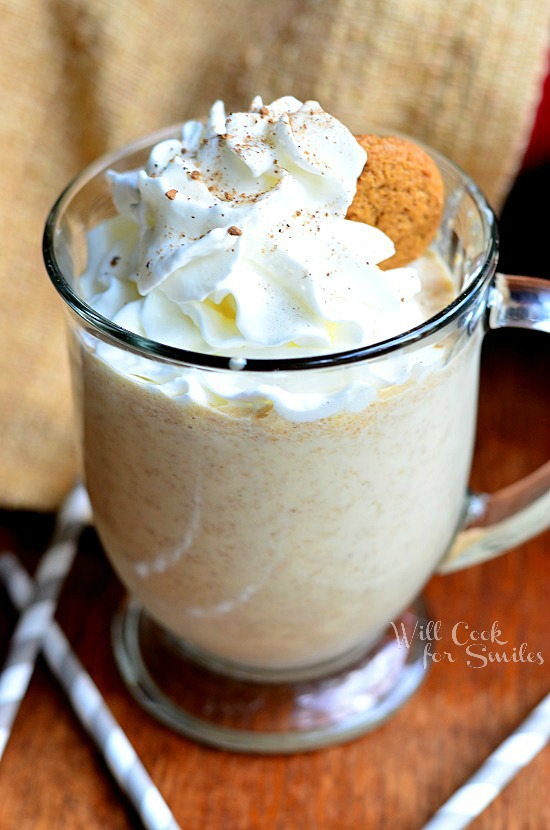 Gingersnap Milkshake in a glass with whipped cream and a ginger bread cookie as garnish on a wood table with white and blue paper straws