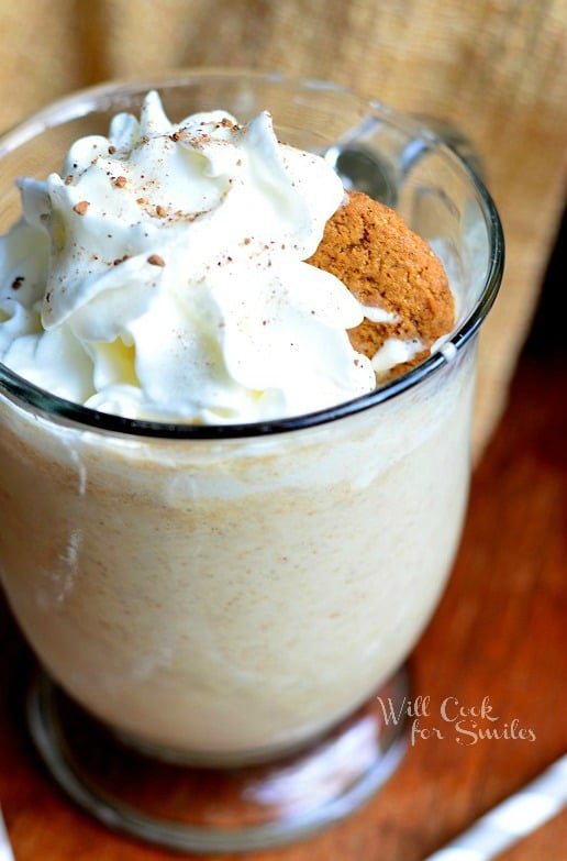 Gingersnap Milkshake in a glass with whipped cream and a ginger bread cookie as garnish on a wood table with white and blue paper straws