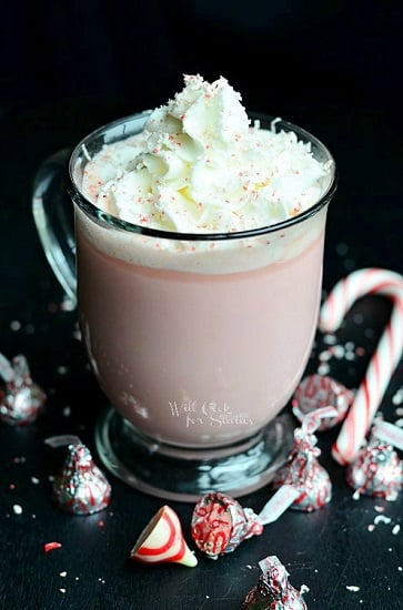 peppermint white chocolate hot chocolate with whipped cream on top and a candy can to the left and peppermint kisses around the bottom