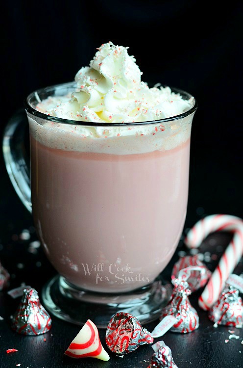 Peppermint White Hot Chocolate in a clear mug with candy canes and peppermint kisses around it