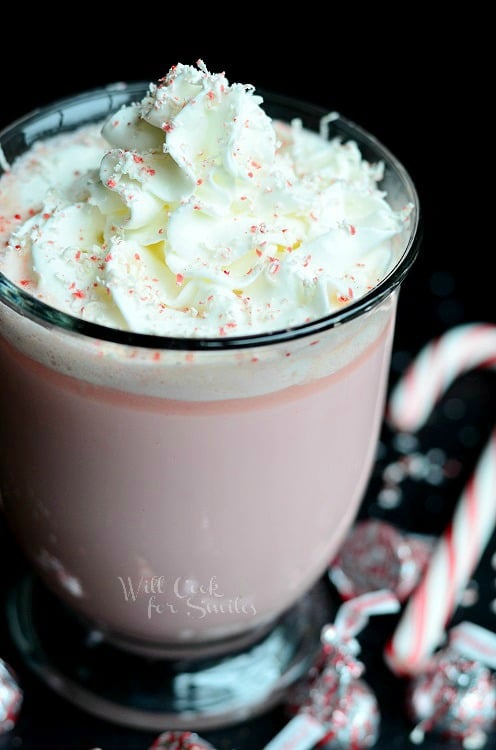 Peppermint White Hot Chocolate in a clear mug with candy canes and peppermint kisses around it