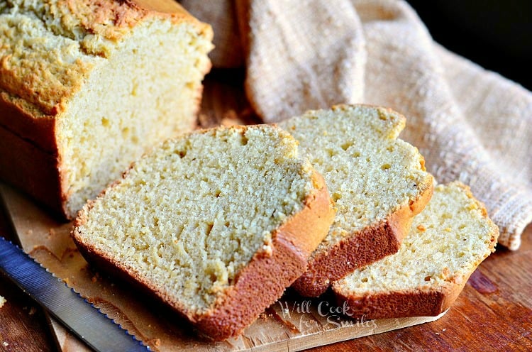 slice of vanilla bean eggnog bread on wood cutting board in front of rest of loaf and brown cloth in background and knife in bottom left