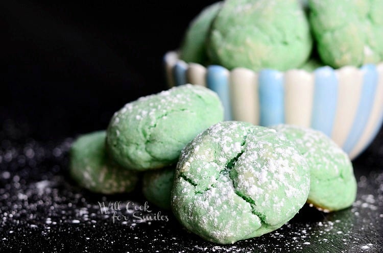 green Cotton Candy Cookies in a black counter top with powdered sugar and a bowl of white and blue cookies