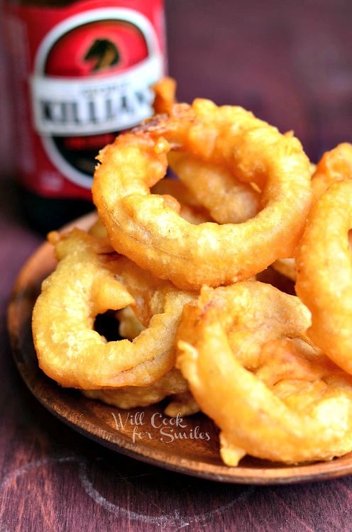 A pile of Beer Batter Onion Rings served on a wooden plate.