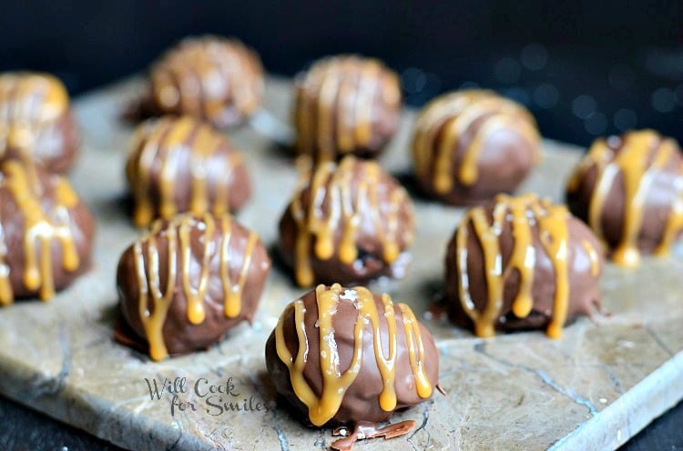 close up view of salted caramel brownie truffles on a stone cutting board each truffle covered in caramel drizzle and salt