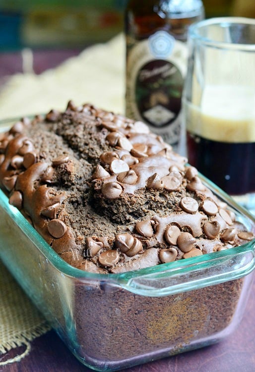 clear glass baking dish with chocolate stout bread on a tan cloth on wood table with clear glass beer mug half full with stout and a bottle of stout in the background