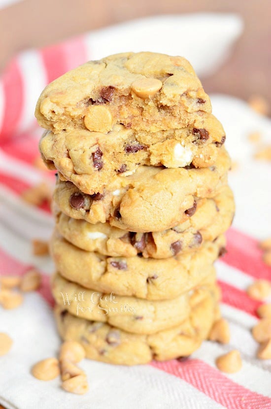 Peanut Butter Cookies that are loaded with white chocolate chips, mini chocolate chips and peanut butter morsels stacked up on a white and red kitchen towel