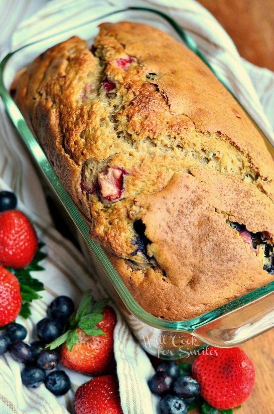 Berry bread in a glass bread pan with blueberries and strawberries on the bottom left