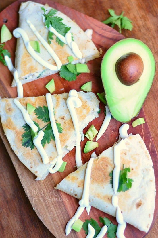 Avocado Chicken Quesadilla on a cutting board with cilantro and sliced avocado on top and half an avocado on the top