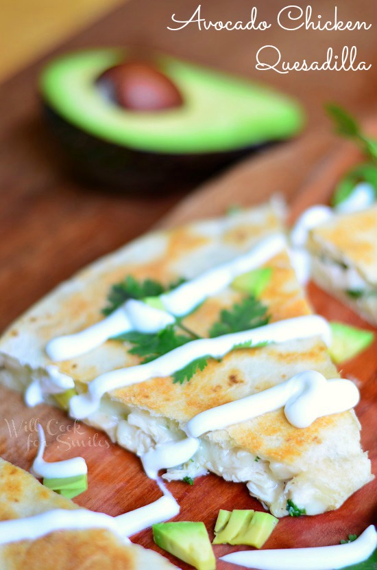 Avocado Chicken Quesadilla with sour cream drizzle on a wood cutting board with half an avocado in the background