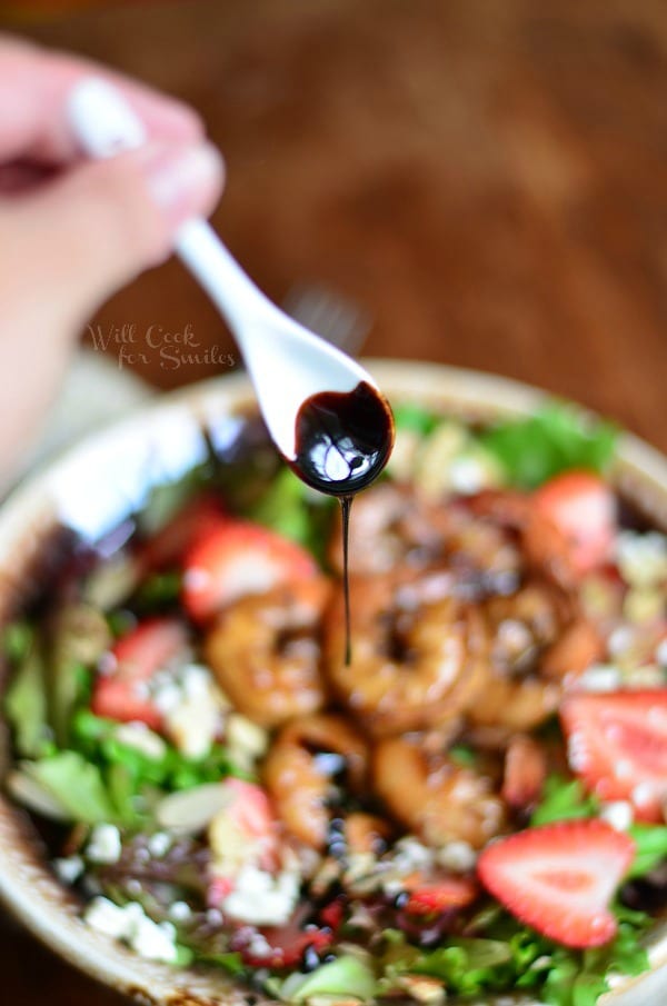 drizzling balsamic reduction over salad with a small white spoon