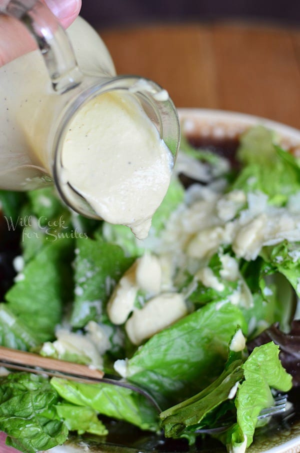 Caesar Dressing in a salad dressing Cruet being poured over salad above that is in a bowl