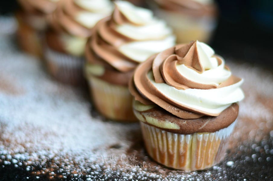 Marble Cupcakes in a row on a black counter top with powdered sugar sprinkled on the counter