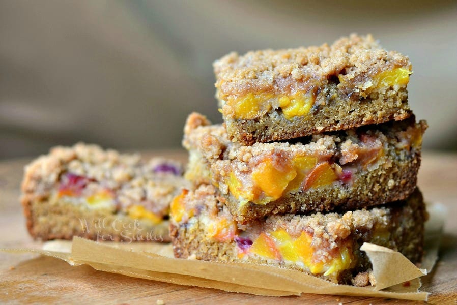 3 peach crumble cookie bars stacked on a brown piece of wax paper on a wooden table