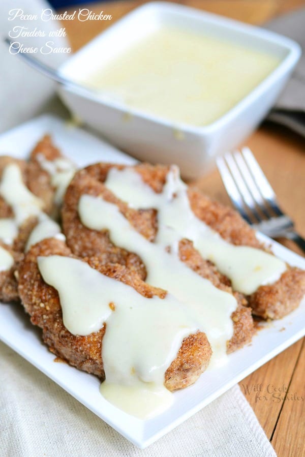 Pecan Crusted Chicken Tenders with Cheese Sauce over them on a white plate and the rest in a small bowl