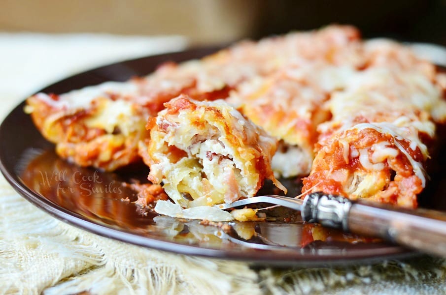 fork with portion cut of manicotti on black plate with 3 pieces in background on plate as well.