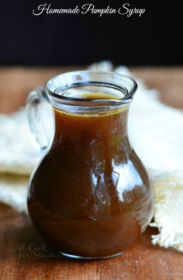syrup jar filled with homemade pumpkin syrup on a wooden table with a white cloth in the background