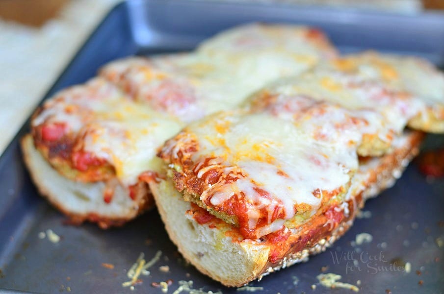 close up view of open faced baked eggplant parmesan sub on a baking pan on tan placemat on wood table