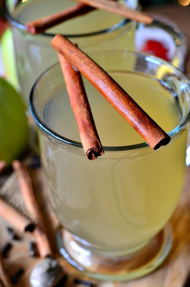 Green Apple Cider in a clear glass with cinnamon sticks over the top