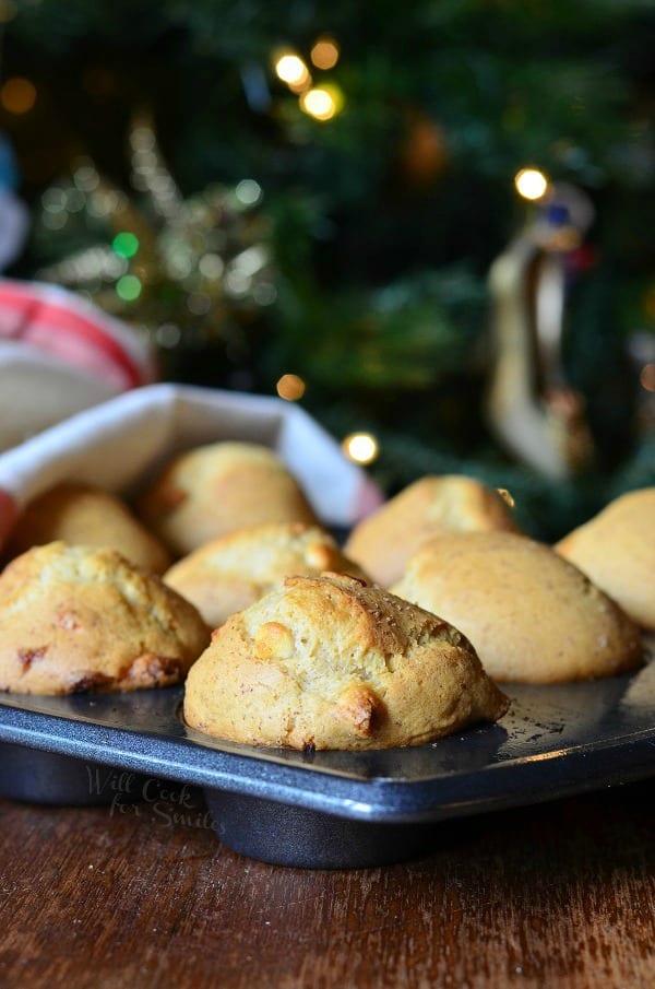 muffin baking pan with white chcolage chip eggnog muffins on a wooden table in front of a christmas tree and a white and red cloth