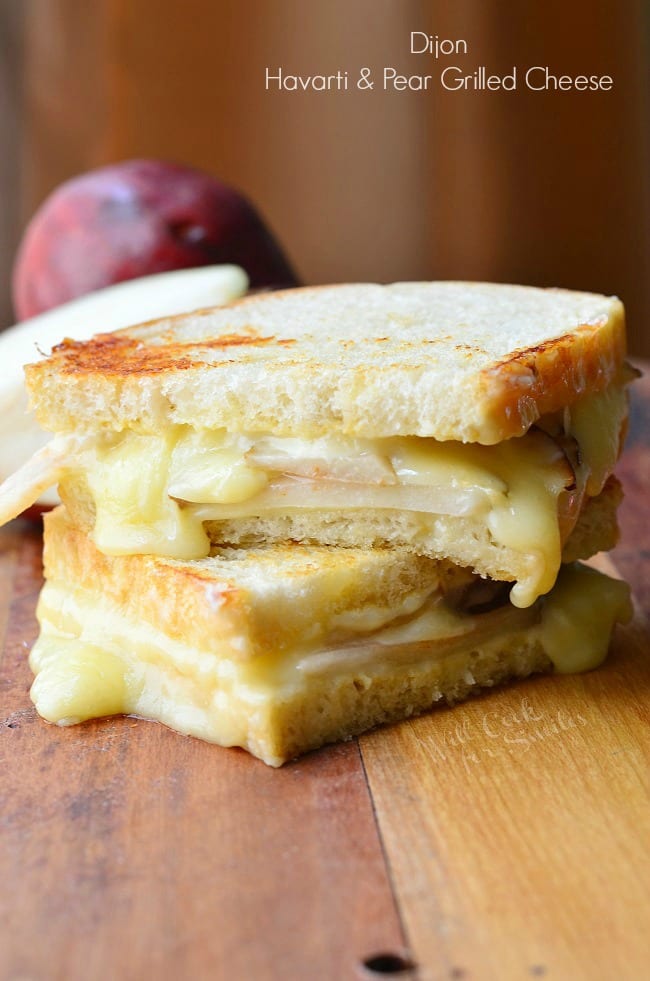 view from the front of a dijon havarti pear grilled cheese sandwich cut in half with the 2 halves stacked on each other on a wood table with a pear in the background