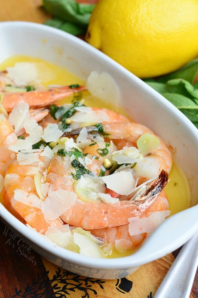 Garlic Sage Butter Shrimp dish in a white baking dish with a lemon on the table beside dish