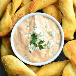 Viewed from above of white crock filled with creamy buffalo dipping sauce surounded by homemade soft pretzel twists