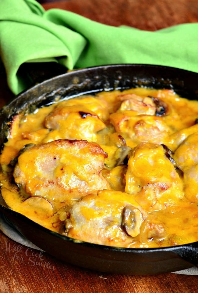 Black skillet with spicy honey mustard chicken on a wooden table with a green cloth in the background.