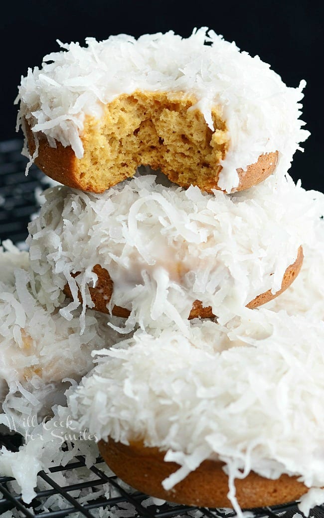 Coconut Cake Donuts with coconut on top stacked up with a bite out of the top one