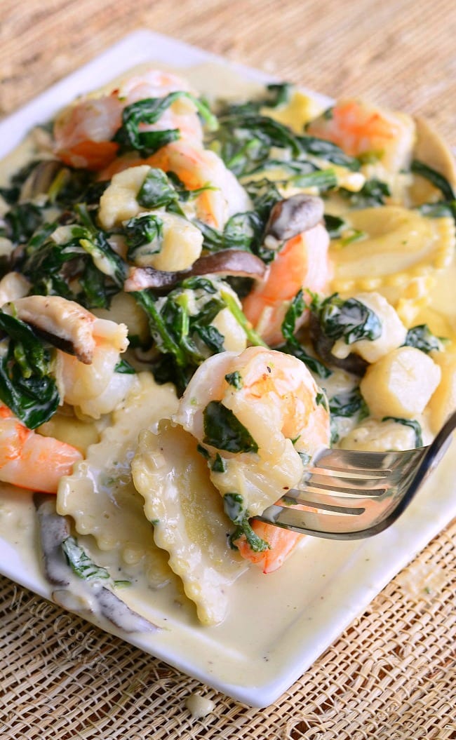 Ravioli with Seafood, Spinach & Mushrooms on a white plate lifting shrimp up with a fork