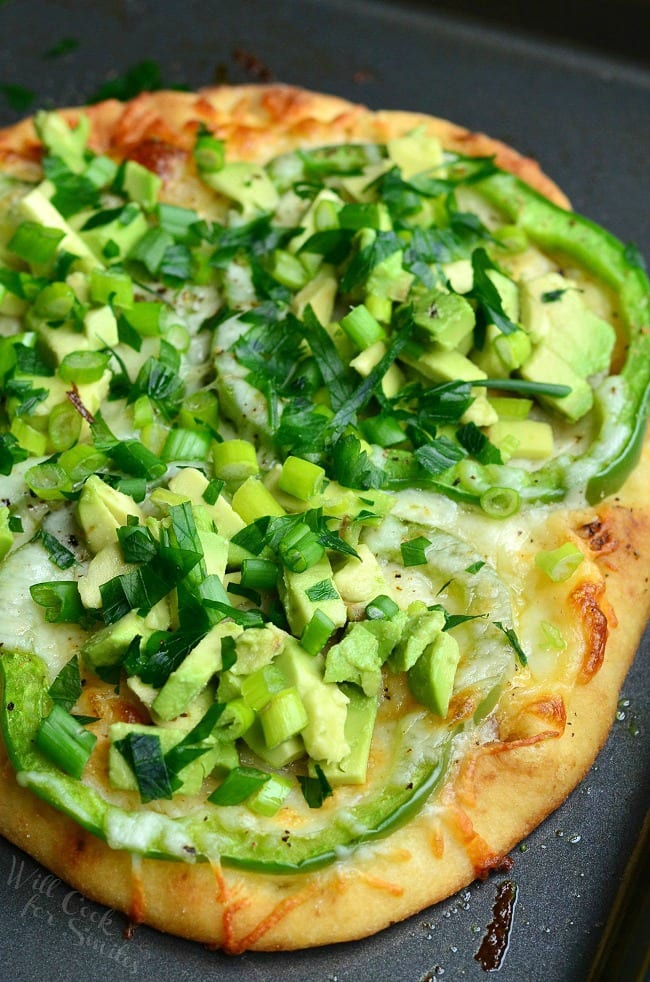 top view photo of Green Naan Pizza with avocado, green peppers and green onions on top.