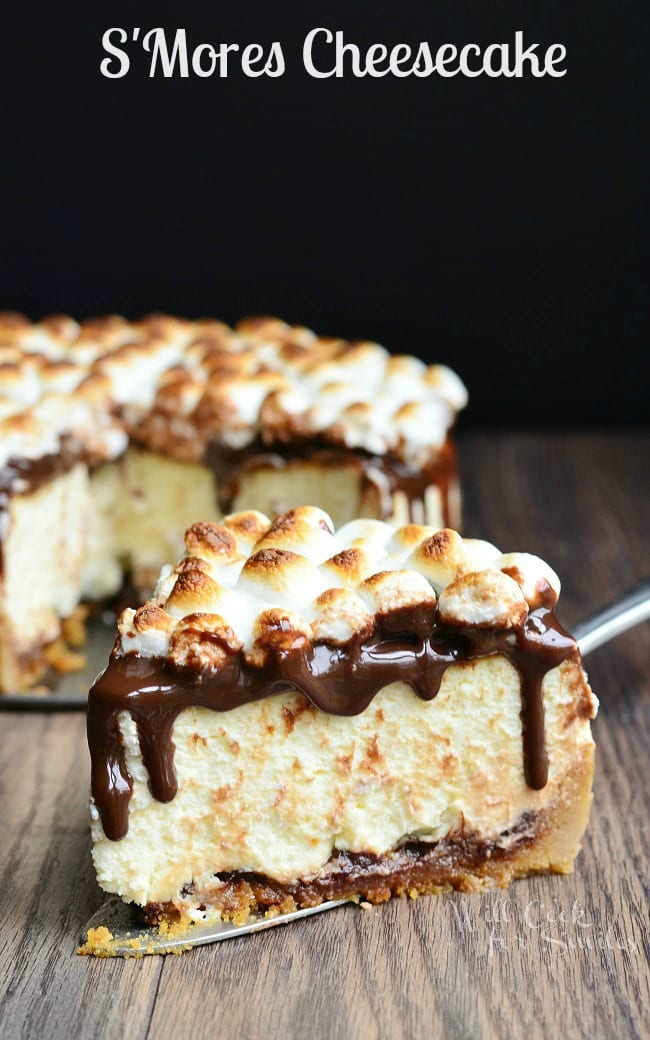 Smores cheesecake on a wooden table with 1 slice on a cake cutter in front of rest of cake