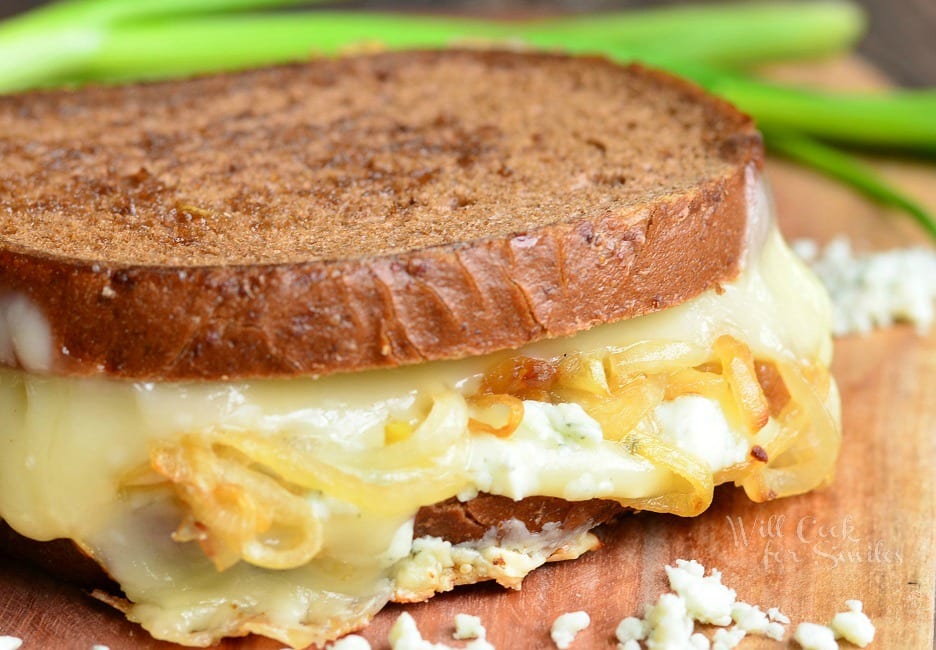 close up of Grilled cheese on a wooden cutting board with blue cheese crumbles in the foreground