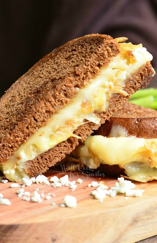 Gruyere and Caramelized Onion Grilled Cheese cut in half and made with Gruyère cheese, blue cheese crumbles and caramelized onions. on a cutting board